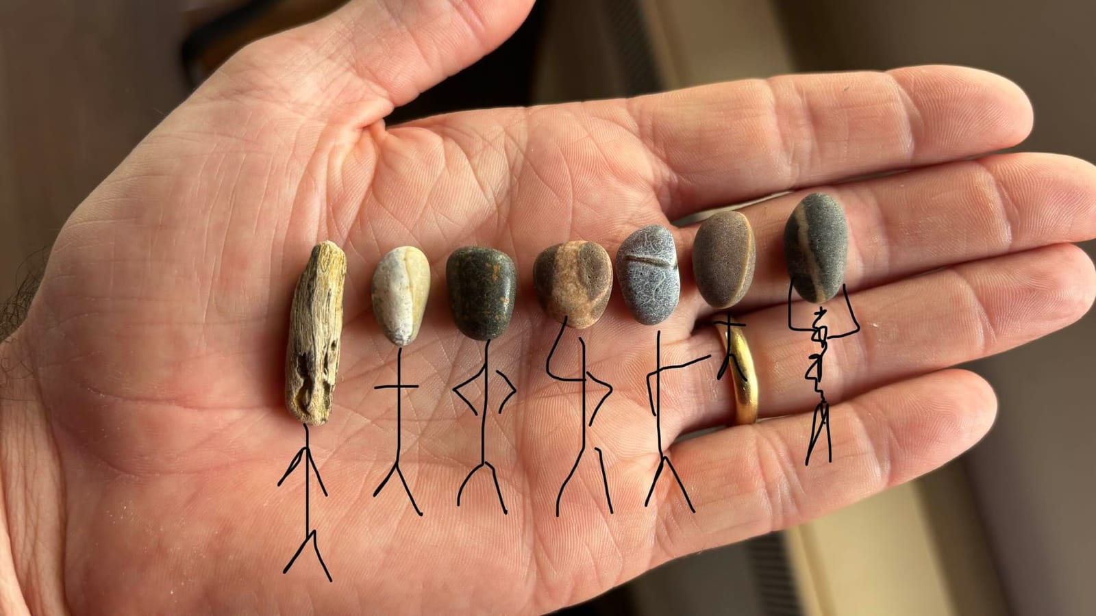 Tiny pebbles and a piece of driftwood on a palm, with stick-figure bodies drawn beneath them